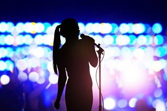 Silhouette of woman with microphone singing on concert stage in front of crowd - Indie Artist